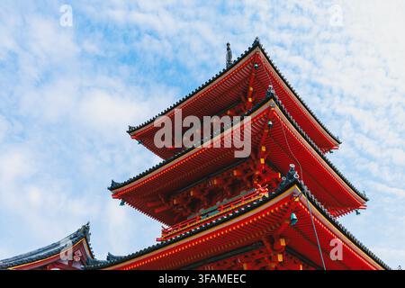 Un drammatico scatto ad angolo basso che guarda verso l'alto ai complessi timpani a più livelli della brillante pagoda rossa a tre piani del tempio Kiyomizu-dera a Kyoto Foto Stock
