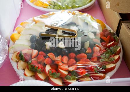Una vivace assortimento di frutti tropicali tagliati tra cui fragole, uva, mele, pere, papaya e mango disposti ordinatamente su un vassoio da portata. Foto Stock
