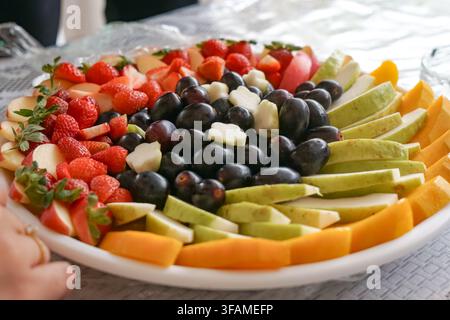 Una vivace assortimento di frutti tropicali tagliati tra cui fragole, uva, mele, pere, papaya e mango disposti ordinatamente su un vassoio da portata. Foto Stock