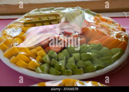 Una vivace assortimento di frutti tropicali tagliati tra cui fragole, uva, mele, pere, papaya e mango disposti ordinatamente su un vassoio da portata. Foto Stock