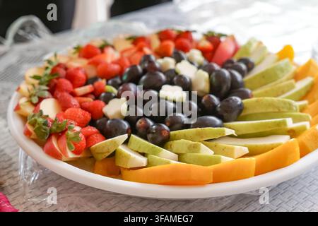 Una vivace assortimento di frutti tropicali tagliati tra cui fragole, uva, mele, pere, papaya e mango disposti ordinatamente su un vassoio da portata. Foto Stock