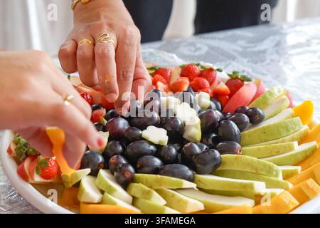 Una vivace assortimento di frutti tropicali tagliati tra cui fragole, uva, mele, pere, papaya e mango disposti ordinatamente su un vassoio da portata. Foto Stock
