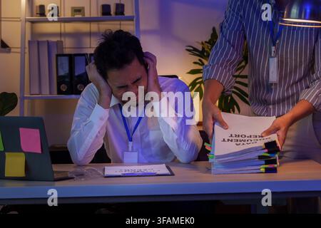Uomo d'affari asiatico stressato sopraffatto da un carico di lavoro extra mentre lavora fino a tardi Foto Stock