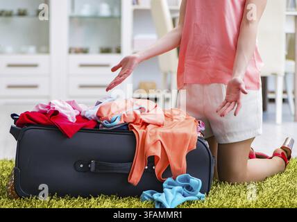 Donna cerca di mettere tutti i suoi vestiti nella valigia prima di andare in vacanza Foto Stock