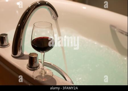 Bicchiere di vino rosso accanto a una vasca da bagno piena di schiuma di bolle. Foto Stock