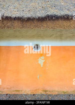 Prima vista di un'abitazione tradizionale ucraina con un tetto di paglia rustico e un muro esterno intonacato di un vivace arancione con una piccola finestra Foto Stock