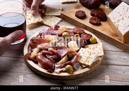 Piatto di tapas spagnole con salumi, formaggio, olive e vino rosso su tavolo di legno Foto Stock