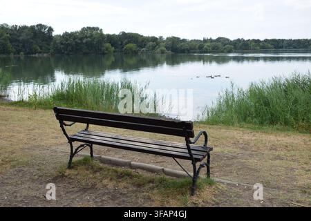 Panchina vuota che si affaccia sul Lago Vecchio a Tata dopo una tempesta estiva, Ungheria... Foto Stock