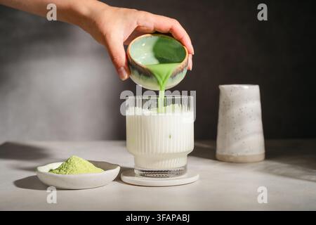 Mano che versa tè verde matcha nella latte fredda Foto Stock