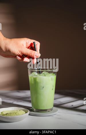 Mano che mescola un cremoso latte freddo al matcha Foto Stock