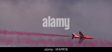 RAF Red Arrows Hawk T1 che vola da solo con una scia di fumo rossa contro un cielo scuro drammatico durante una dimostrazione acrobatica Foto Stock