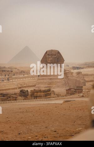 Sphynx sullo sfondo delle Grandi Piramidi Egiziane. Africa, altopiano di Giza. Una tempesta di sabbia nell'aria che conferisce un aspetto arancione al cielo. Foto Stock