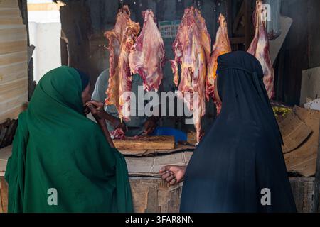 Donne acquistano carne da un venditore nel centro storico di Mogadiscio, Somalia, durante il giorno Foto Stock