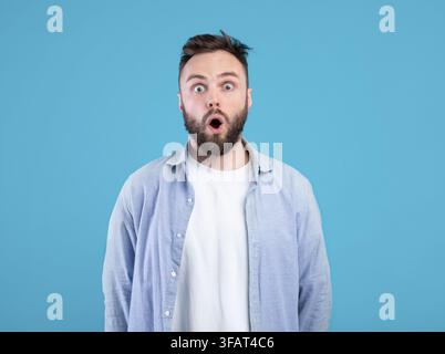 Ritratto di giovane ragazzo stordito apertura bocca in shock su sfondo blu studio Foto Stock