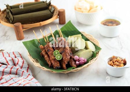 Prima piano di Satay di pollo marinato e grigliato servito su un piatto. Il pollo è carbonizzato e glassato con una salsa saporita e dolce. Ad accompagnare gli spiedini Foto Stock