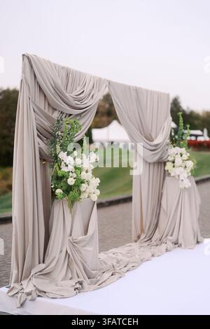 Elegante arcata per matrimoni all'aperto con stoffa drappeggiata e fiori Foto Stock