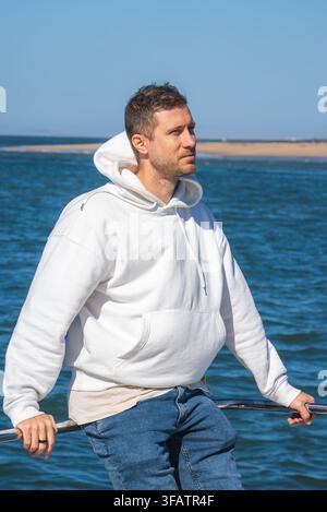 Uomo con una felpa con cappuccio bianca in piedi su una barca sulla costa Foto Stock