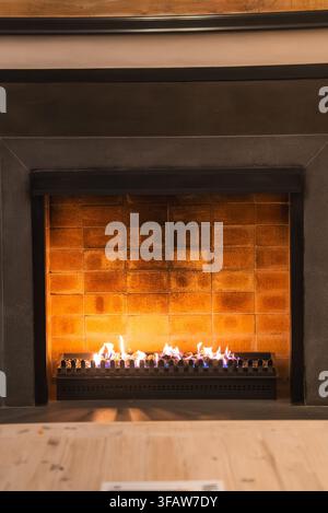 Camino moderno che brucia con fiamme a gas in un interno in mattoni Foto Stock