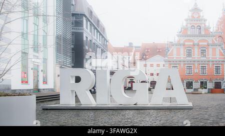 Il branding cittadino visibile si concentra sulle grandi lettere RIGA davanti agli edifici storici e moderni della capitale lettone, offrendo una chiara immagine della destinazione f Foto Stock