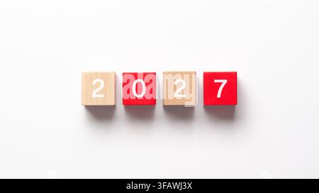 Concetto di Capodanno 2027. Cubi rossi e in legno con i numeri in bianco, su sfondo bianco e spazio per la copia. Foto Stock