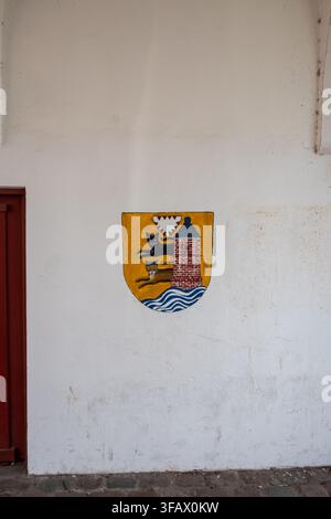 Stemma araldico colorato dipinto su un muro bianco a Flensburgo, con gatti e un faro, ideale per uso editoriale di viaggio e culturale. Foto Stock