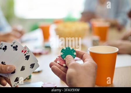 Primo piano di amici che giocano a poker con carte e fiches a un tavolo da festa con bevande Foto Stock