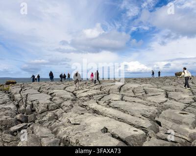 Turisti che camminano nel Burren, paesaggio carsico/glaciolo-carsico, formazioni rocciose nella contea di Clare, costa occidentale dell'Irlanda Foto Stock