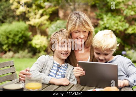 Nonna, bambini e tablet all'aperto con il sorriso per giochi online, intrattenimento e legame. Donna matura, nipoti maschi e felici con la tecnologia Foto Stock