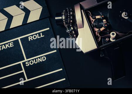 Macchina da presa vintage e clapperboard su sfondo nero, primo piano. Vista dall'alto di una macchina da presa retrò aperta con bobina di film accanto a clapperboard nero Foto Stock
