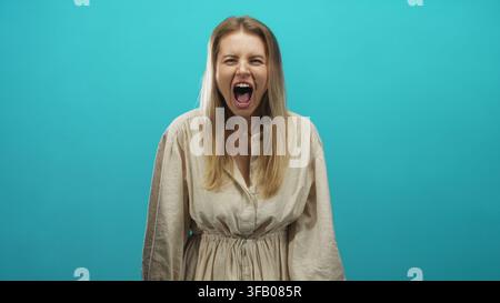 Donna con bocca aperta che urla, denti e mani visibili, faccia espressiva sullo sfondo turchese dello studio; rilascio della rabbia. Foto Stock