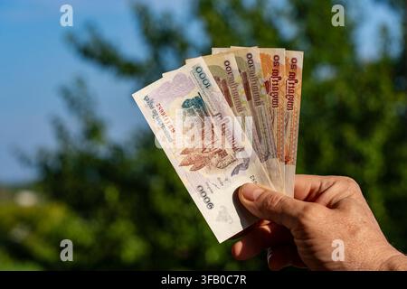 Uomo che tiene banconote di riel cambogiano in mano all'aperto. Primo piano di una mano che tiene diverse banconote di riel cambogiano di diverse denominazioni contro b Foto Stock