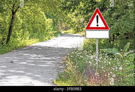 Un cartello di avvertimento triangolare con punto esclamativo si trova accanto a una strada rurale stretta e tortuosa circondata da alberi verdi rigogliosi e fiori selvatici, segnalando ca Foto Stock