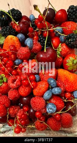 Assortimento colorato di fragole, lamponi, mirtilli, more e ciliegie disposte come un mix di frutti di bosco freschi. Foto Stock