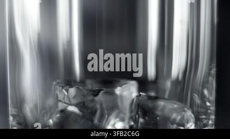 Cubetti di ghiaccio all'interno di un bicchiere trasparente che mostra riflessi astratti e un liquido monocromatico Foto Stock