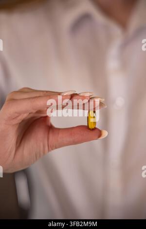Donna che tiene in mano una capsula dorata di integratore alimentare Foto Stock
