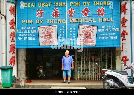 Uomo in piedi davanti alla vetrina della farmacia tradizionale cinese Pok Oy Thong Medical Hall con cartello blu a Penang, Malesia Foto Stock