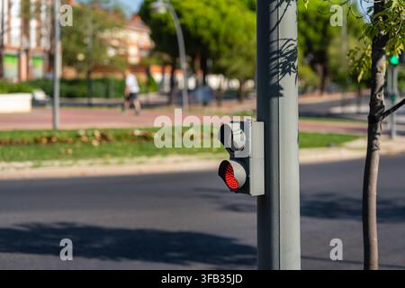 Piccolo semaforo rosso accanto a una strada urbana con alberi e un corridore sfocato sullo sfondo Foto Stock