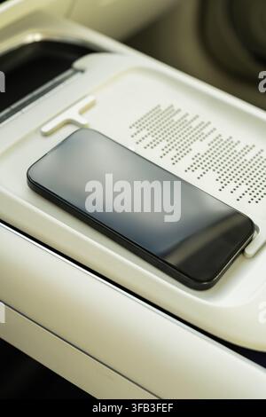 Primo piano di uno smartphone appoggiato su un pad di ricarica wireless nella console centrale di un'auto elettrica, evidenziando la connettività moderna, la potenza della batteria e cl Foto Stock