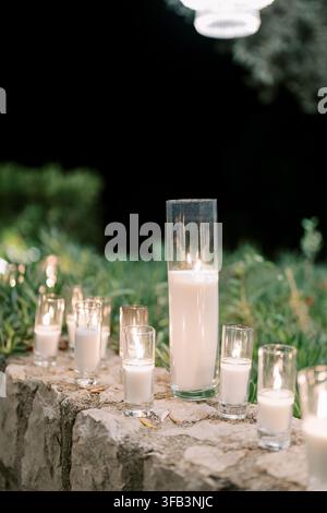 Diverse candele bianche in portacandele di vetro su un muro di pietra di notte Foto Stock