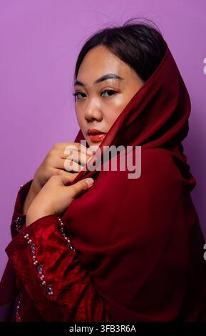 Ritratto di una giovane donna musulmana asiatica che indossa un hijab marrone su uno sfondo viola Foto Stock