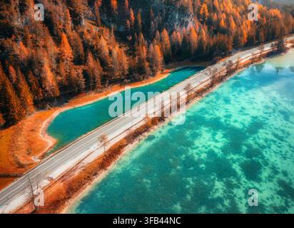 Vista aerea di una strada lungo un lago alpino turchese e alberi autunnali Foto Stock