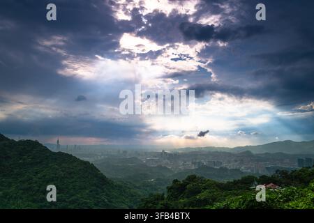 Raggi di sole drammatici che penetrano attraverso nuvole tempestose scure e drammatiche sopra le montagne verdi lussureggianti e lo skyline della città di Datianjian a Nuovo Taipei, Taiwan Foto Stock