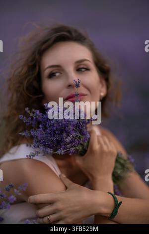 Ritratto di un campo di lavanda con una giovane donna che tiene fiori di Lavandula viola durante il tramonto estivo Foto Stock