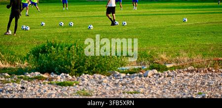 Una foto orizzontale di una sessione di allenamento di calcio su un campo verde con diverse palle e giocatori che si allenano sullo sfondo. Foto Stock