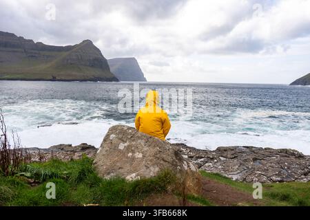 Persona in giacca gialla che contempla la vista sull'oceano nelle Isole Fær Øer Foto Stock