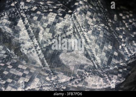 Un tessuto tessile argentato a quadri con trama stropicciata e superficie riflettente che crea uno sfondo astratto in primo piano Foto Stock