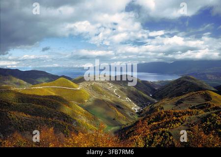 Coline autunnali dorate con strada di montagna tortuosa che si affaccia sul lago di Ocrida, cielo nuvoloso drammatico. Pogradec, distretto di Korçë, Albania, Europa Foto Stock