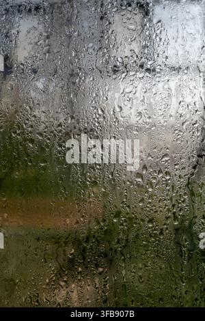 Gocce di pioggia cadono su un vetro della finestra durante una giornata nuvolosa Foto Stock