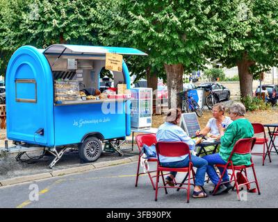 Carrello mobile per caffè e snack parcheggiato nella piazza del paese con persone sedute su sedie e tavoli - Beaulieu-lès-Loches, Indre-et-Loire (37), Francia. Foto Stock
