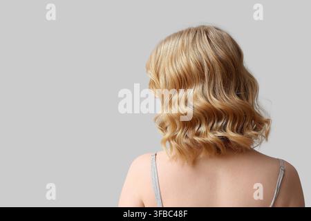 Concetto di cura dei capelli e bellezza, vista posteriore di una donna con capelli biondi ondulati sani, acconciatura corta su sfondo grigio Foto Stock